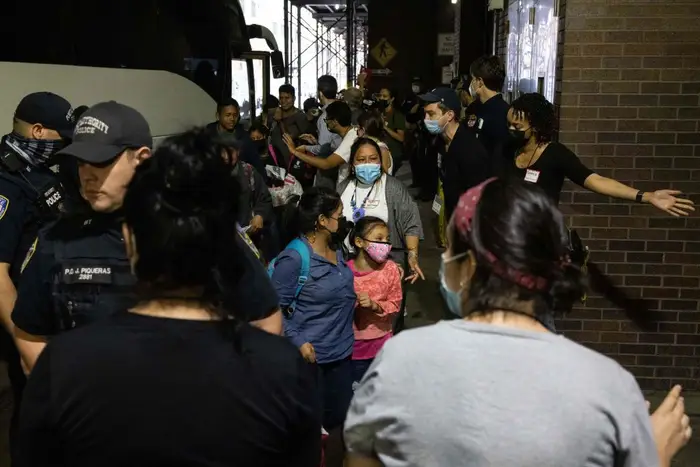Law enforcement surrounds a group of migrants getting off a bus at the Port Authority, including a young girl wearing a pink mask.